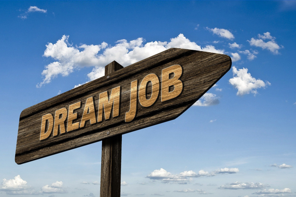 A wooden road sign on the shape of an arrow with Dream Job written on it