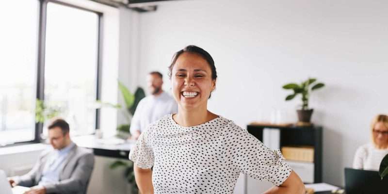 Hire marketing apprentice Woman in an office smiling broadly at camera in a casual pose wearing a white t-shirt with black spots