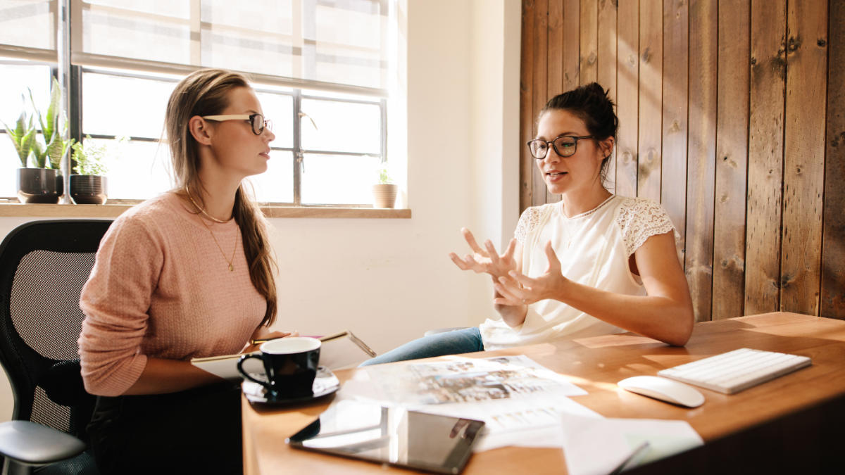 Two young female creative professionals discuss and idea. They are dressed casually and wearing glasses